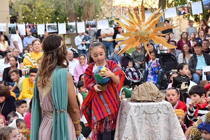 Students from Mountain West Montessori in El Paso are holding a globe and wearing scarves. They are involved in educational activities such as attending international ballet performances at UTEP and visiting a local pumpkin farm