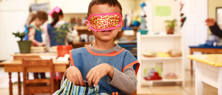 A child with a blindfold is feeling sensory materials to enhance sensory development inside the children’s house at Mountain West Montessori