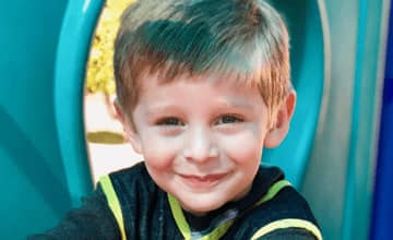 Little boy smiling while wearing a black and yellow striped shirt, with a blue slide in the background at Mountain West Montessori in El Paso