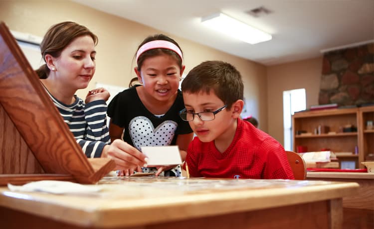 A teacher is performing at the desk while the young children watch inside Mountain West Montessori