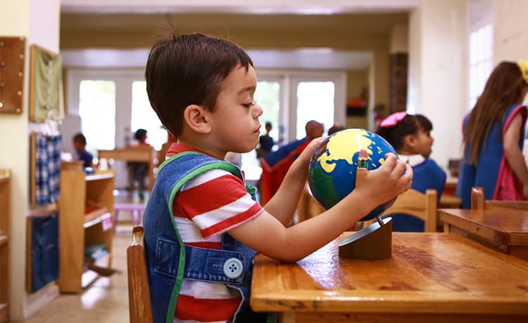 A boy studying in a Mountain West Montessori classroom in El Paso, holding a globe in his hands